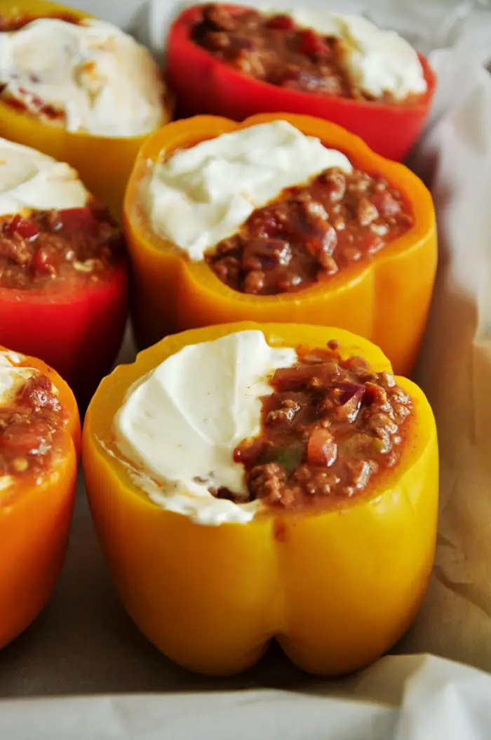 Stuffed peppers with taco-flavored ground beef, onion, tomatoes and cheddar cheese topped with avocado slices, fresh cilantro, and sour cream. Find the updated recipe and cooking video at https://www.delishplan.com/taco-stuffed-peppers.