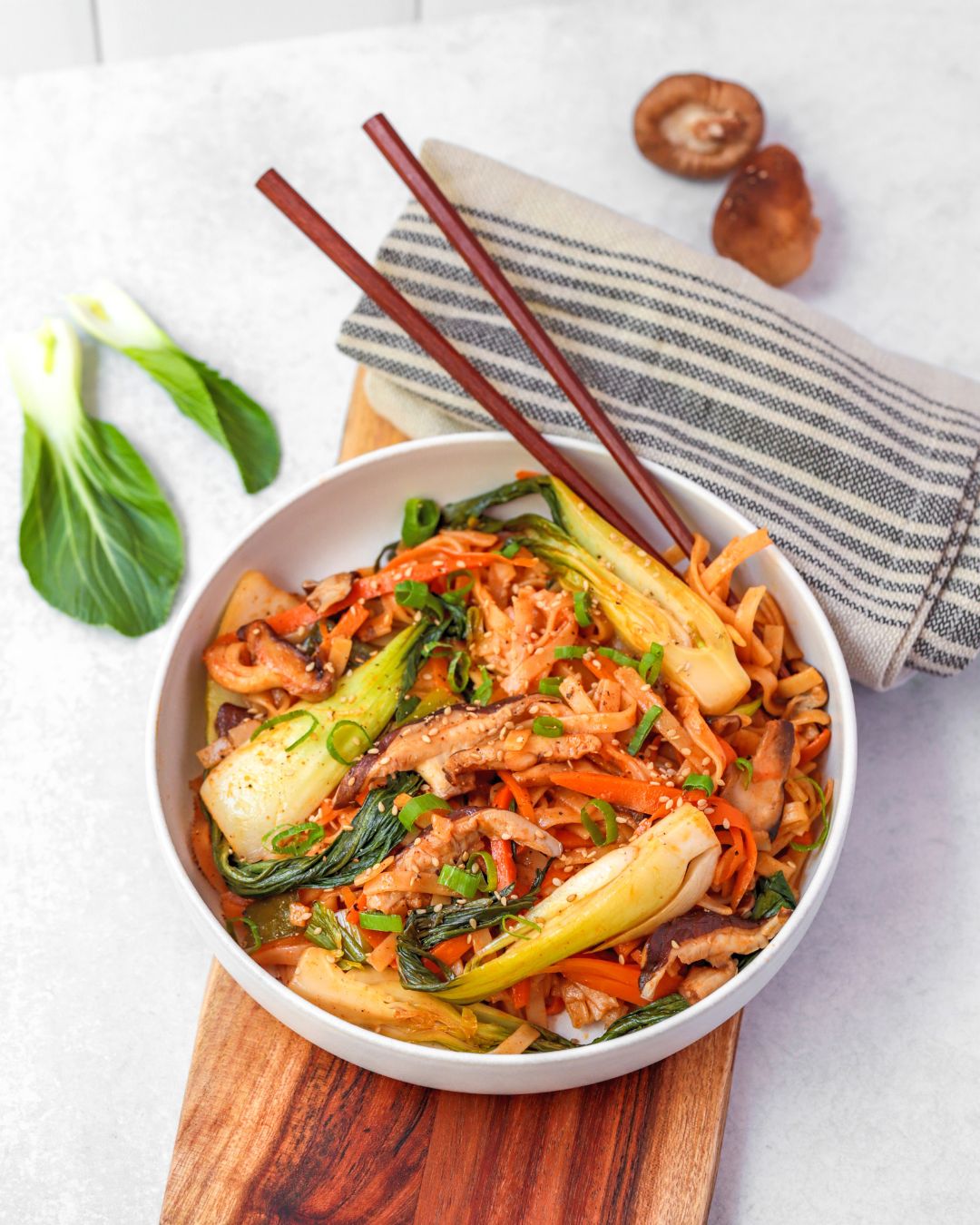 This quick and easy plant-based meal cooked in a delicious Korean stir-fry sauce features Asian mushrooms, carrots, bok choy, and rice noodles.