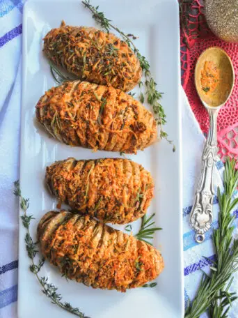 Perfectly baked hasselback potatoes with garlic slices in between, brushed with infused butter, topped with cheddar, parmesan, and three freshly chopped herbs.